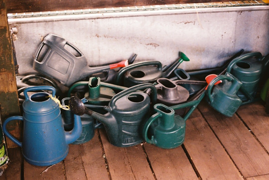 A pile of plastic watering cans in blue, green, and grey on wooden floorboards